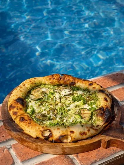 A delicious-looking pizza right by the pool. This shot creates a perfect holiday or vacation vibe, blending delicious food with a relaxed, aspirational setting.