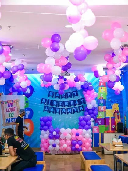 A full view of a party room decorated in pink and purple. Our team transforms the space with elaborate balloon displays hanging from the ceiling and around the cake table.