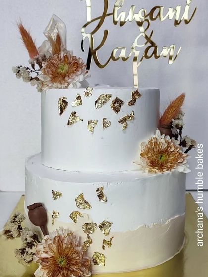 A rustic and chic two-tiered wedding cake with dried flowers and gold leaf.