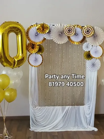 A simple and elegant 50th birthday setup with large foil number balloons and a photo backdrop made of drapes and paper fans.