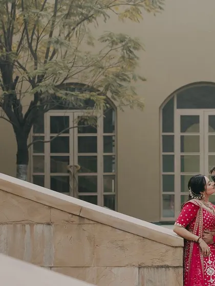 A romantic kiss against a beautiful architectural backdrop. The vibrant pink of their outfits stands out, creating a striking and joyful image that celebrates their love.