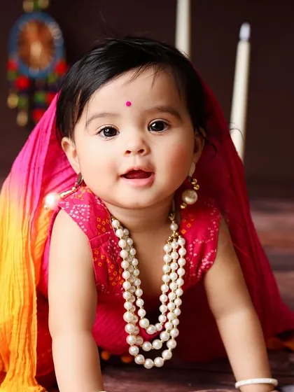 This crawling baby girl looks adorable in her traditional Indian attire, smiling brightly for the camera.