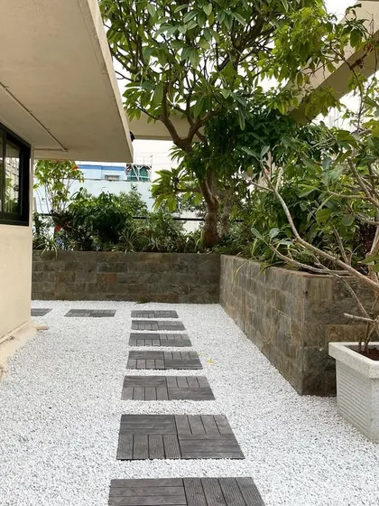 A daytime view of the corporate terrace, highlighting the contrast between the white gravel ground cover and the dark wood stepping stones. The mature trees in the planters provide shade and a sense of establishment.
