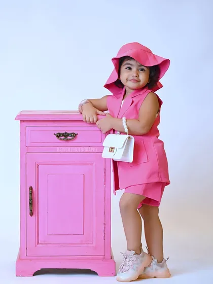 A fashionable kid's portrait, with a little girl dressed in a stylish pink outfit and hat.