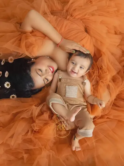 An aerial view of a mother and her smiling baby lying together on a sea of orange tulle, creating a warm and joyful image.