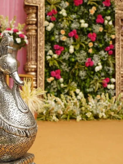 Details matter. The intricate carving on the silver peacock prop contrasts beautifully with the soft petals of the floral wall behind it.