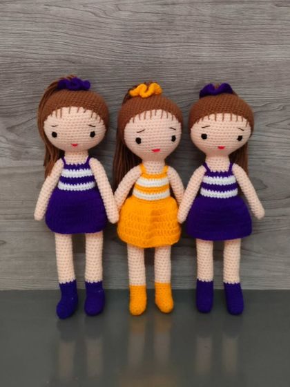 A group of three dolls, two in purple and one in a matching orange dress.
