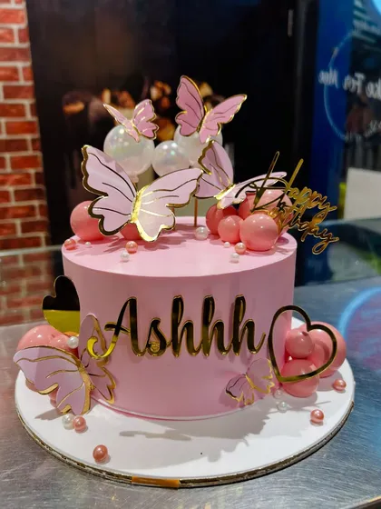 A chic pink birthday cake decorated with elegant pink and gold butterflies and decorative spheres.