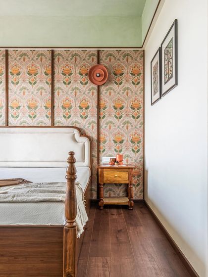 This master bedroom is a tribute to traditional Indian craftsmanship. The bed features classic turned wood posts, and the wall behind it is adorned with a beautiful floral wallpaper, framed by wooden panels to create a bespoke feature.