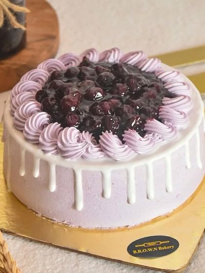 A full view of our Exotic Blueberry Cake, with a white chocolate drip and a generous topping of our house-made blueberry compote.
