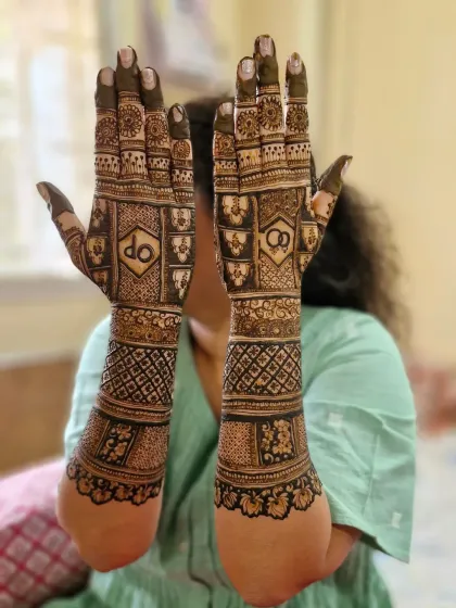 This full-arm engagement mehendi showcases the couple's initials 'DP' and interlocking rings. The design is packed with geometric patterns and floral details.