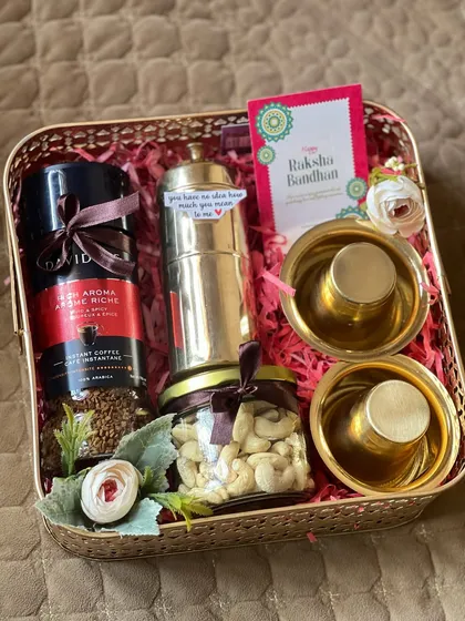 This Rakhi hamper, set in a stylish gold metal basket, is a sophisticated gift for a coffee lover. It includes premium coffee, a traditional filter, cashews, and brass tumblers, blending modern taste with festive tradition.