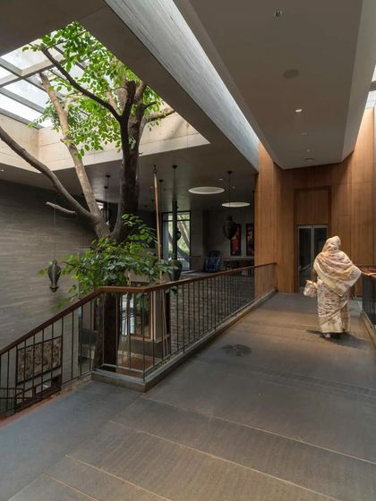 A sky-lit internal bridge in the Maheshwari house in Pune passes by a mature tree growing within the home, creating a powerful connection to nature.