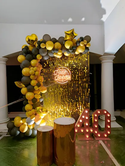 A glamorous 40th birthday setup with a gold sequin wall, a yellow and grey balloon arch, and large marquee numbers.