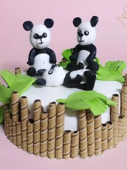 A playful panda cake made with fondant. This design features three pandas surrounded by bamboo-style wafer rolls and green leaves.
