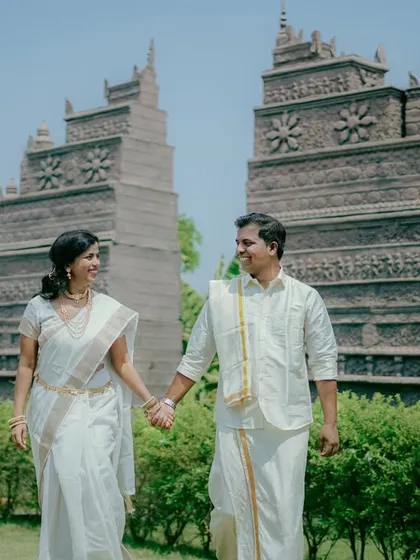 A grand and beautiful shot of Aditya and Priyanka in traditional South Indian attire, walking hand-in-hand against a stunning temple-like backdrop.