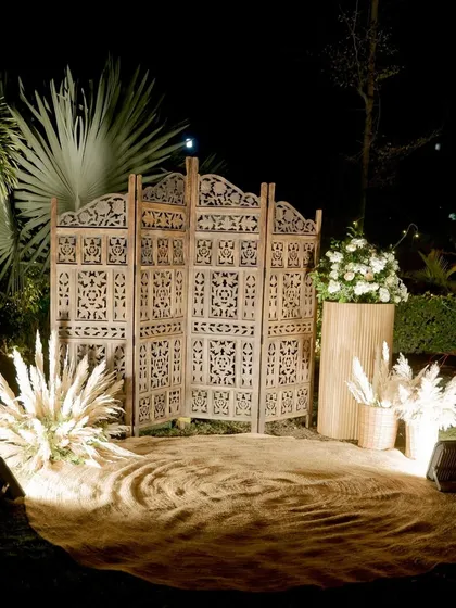 A cozy and rustic photo corner we created with a carved wooden screen, pampas grass, and jute fabric, perfect for capturing memories at the 25th anniversary party.