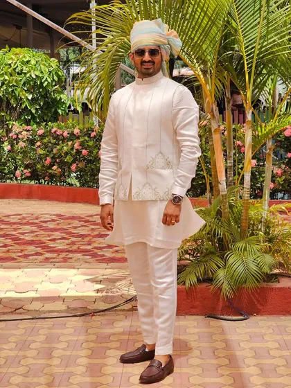 A client looking sharp and ready for a celebration in an off-white, subtly embroidered jacket and kurta set, complete with a colorful turban. This is a perfect wedding guest outfit.