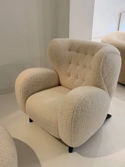 A modern, sculptural armchair upholstered in a cozy bouclé fabric. The rounded, organic shape and button-tufted back make it a comfortable and eye-catching accent piece.