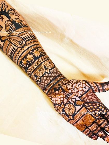 A close-up of a bridal arm design, featuring a peacock under a tree, showcasing the fine line work.