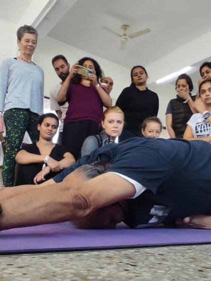 Demonstrating Karnapidasana (Ear Pressure Pose) to a group of students. This deep forward bend calms the nervous system and stretches the entire spine.