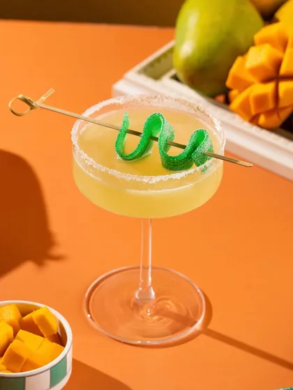 A mango margarita with a fun, curly green garnish. The bright, contrasting colors make this shot playful and eye-catching.