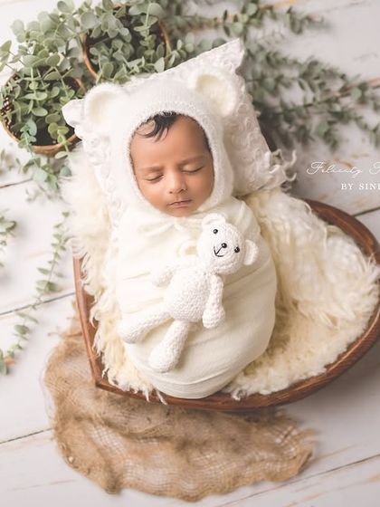 A top-down view of a newborn nestled in a heart-shaped bowl, dressed as a tiny bear. This creative pose is done with the utmost care and safety.