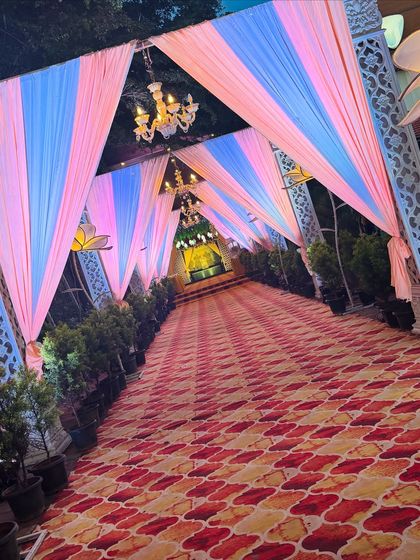 A beautiful walkway at dusk, with pastel pink and blue drapes illuminated by chandeliers. The design creates a soft, romantic ambiance, perfect for welcoming guests to an evening celebration.