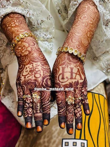 A beautiful shot of the developed henna stain, adorned with bridal jewelry. The design includes the initials 'H' and 'A'.