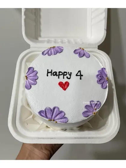 An elegant anniversary cake with the message 'Happy 4' surrounded by hand-piped purple flowers with gold centers.