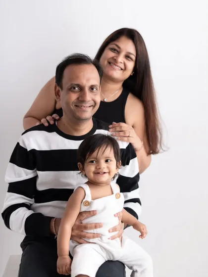 A happy family of three. This studio portrait showcases a classic pose that is perfect for capturing a smiling baby sitting comfortably with mom and dad.