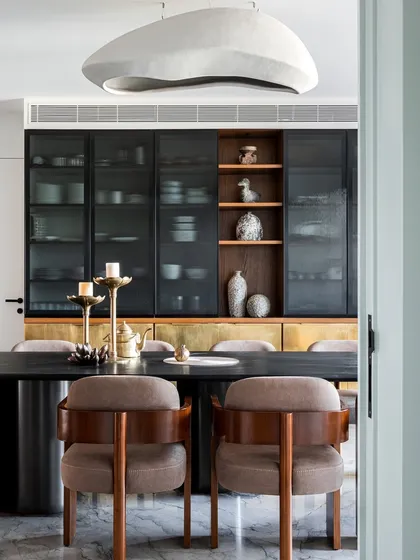 For me, a dining room is a stage for connection. Here, custom storage with fluted glass and brass shutters offers both style and function, while the sculptural pendant light casts a warm glow, creating a space that is both elegant and inviting for family gatherings.