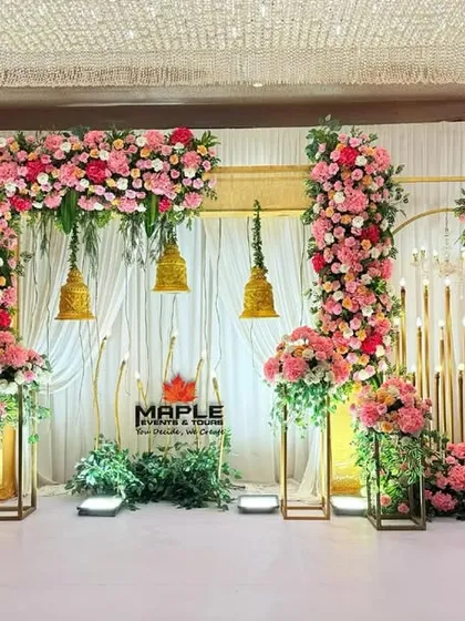 A beautiful blend of gold structures and pink floral arrangements for a romantic wedding stage. The hanging temple bells and warm lighting add a traditional touch to this elegant and modern setup.