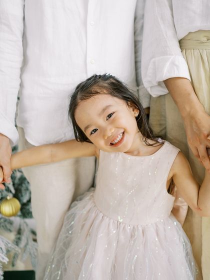 A little girl holding her parents' hands, with a big smile. A happy and bright holiday portrait.