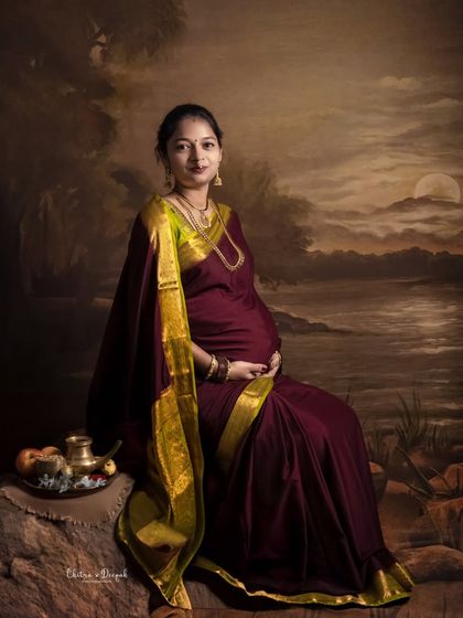 A fine-art portrait inspired by classic paintings. The mom-to-be in her saree looks serene and timeless against the painted landscape backdrop.