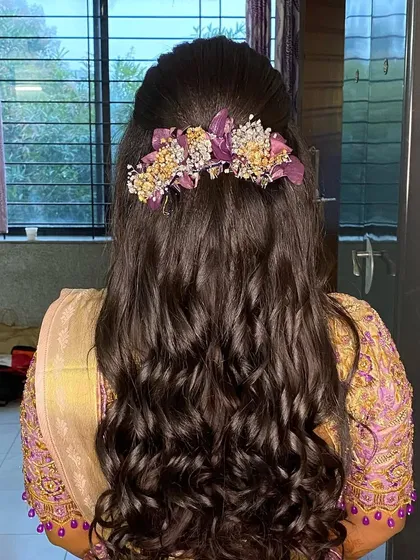 This reception look features a half-updo with soft curls and a beautiful floral accessory. The purple flowers perfectly match the bride's outfit.
