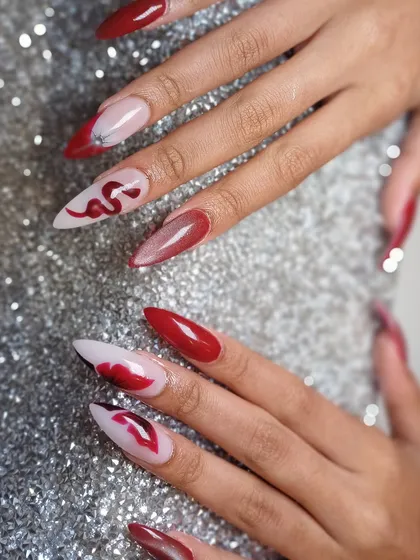Slay your day with these fierce red and black nails, featuring hand-painted snakes and lips for a bold, edgy vibe.