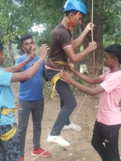 Instructors help a participant get into his harness for a rope activity, ensuring all safety checks are complete.