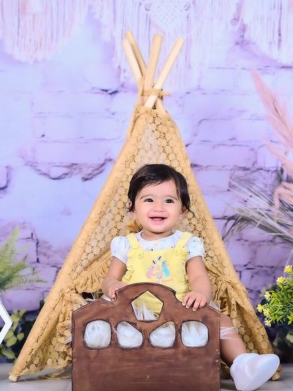 A smiling baby in a teepee setup with bohemian-style decor.