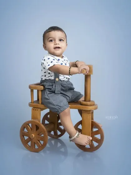 A classic toddler portrait on a wooden tricycle. The simple blue background and the child's direct gaze make for a clean and engaging photograph.