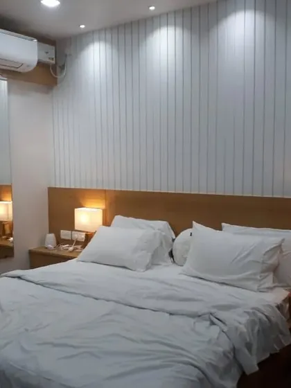 This bedroom demonstrates our approach to creating serene and restful spaces. We installed a custom white vertical-paneled wall to add texture and height, complemented by a warm wood headboard and matching side tables with soft, ambient lamps for a calm, hotel-like feel.