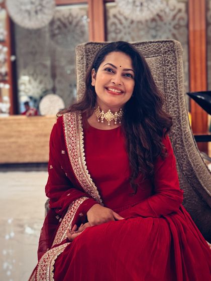 A close-up portrait of Priyanka Barve in her red Anarkali, her smile lighting up the frame.