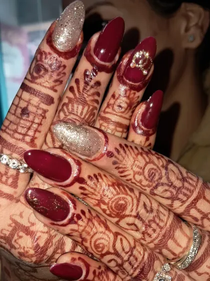 We love how these bridal nails look with the intricate mehndi design. This set features a deep maroon polish on long almond nails, with two accent nails in a sparkling champagne glitter and a small bow charm.