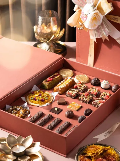 An open view of a luxurious pink gift box, revealing an assortment of handcrafted Belgian pralines, financier bars, mini tarts, and other bite-sized desserts. This gives a close-up look at the intricate and diverse patisserie I create for the festive season.
