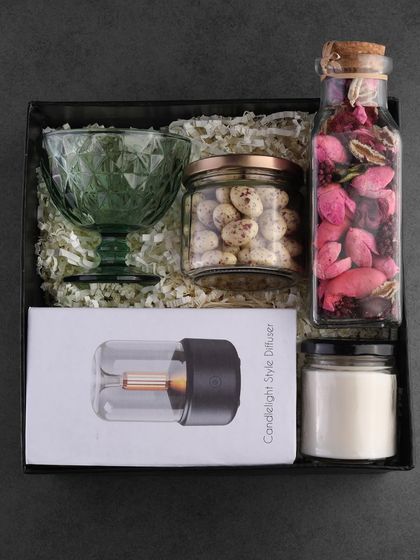 This luxury hamper is designed for relaxation. It features a candlelight-style diffuser, a beautiful green glass dessert bowl, a jar of potpourri, a jar of coated nuts, and a scented candle.