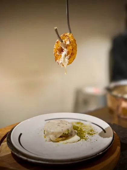 This Cheesy Donut is pure indulgence. It’s a golden-fried, savory donut filled with molten cheese, served dramatically off a hook and finished with a fragrant basil crumble. The drip of the cheese promises a rich and satisfying experience.