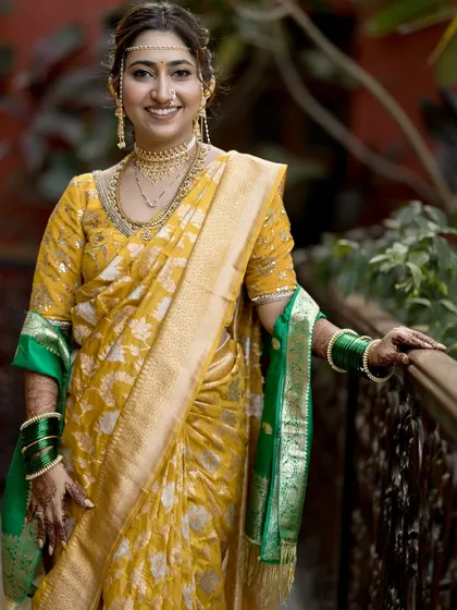 This beautiful Maharashtrian bride is glowing in a golden-yellow saree with a green border. Her look is traditional, complete with a mundavalya and nath.
