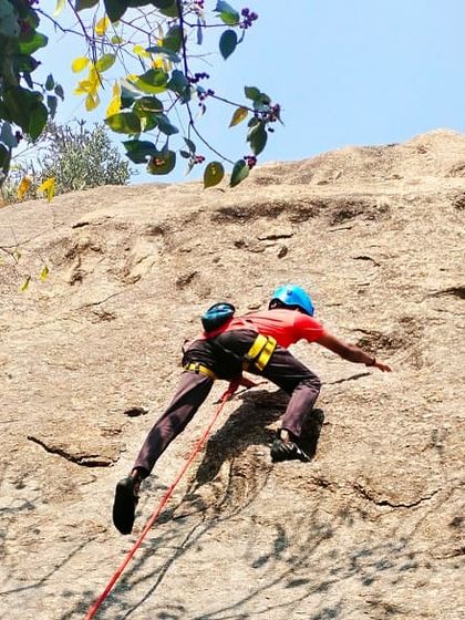 A climber fully equipped with a helmet and harness tackles a top-rope climb. The rope running through an anchor at the top ensures a safe and controlled environment for learning.
