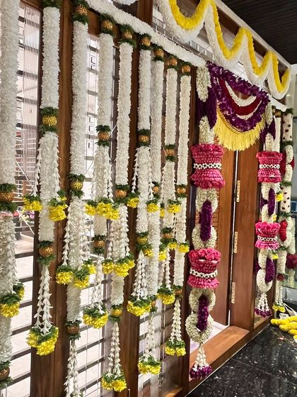A beautifully decorated doorway in a modern home. The combination of traditional flower garlands in vibrant colors adds a festive and welcoming touch to the housewarming celebration.