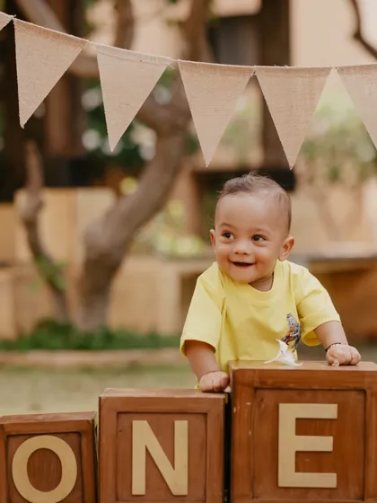 A happy, candid moment from a first birthday photoshoot. The rustic 'ONE' blocks and outdoor setting create a perfect backdrop for capturing this little one's joyful smile.